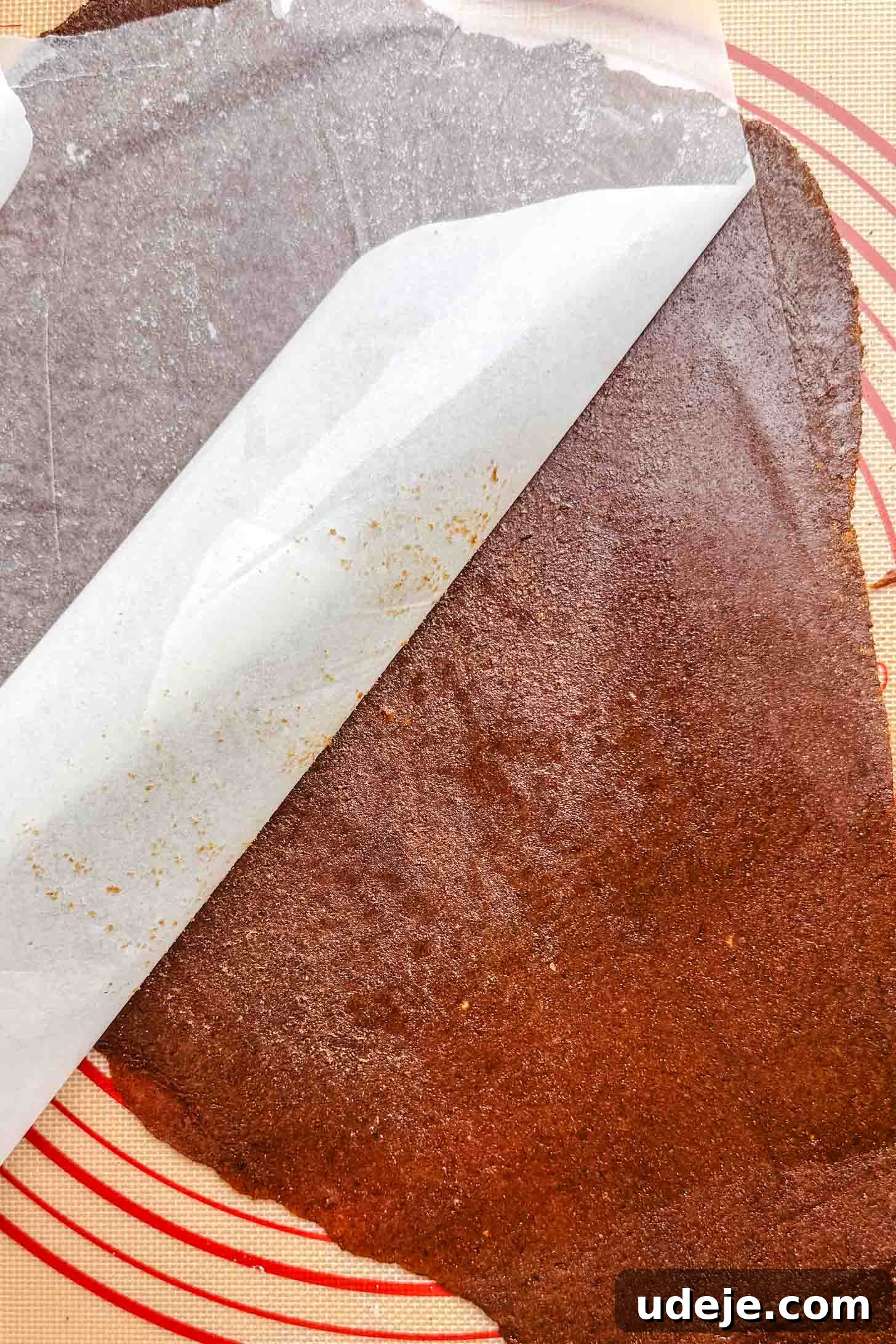Iraqi Kleicha A Sweet Tradition with Date or Walnut 13 A sheet of dark brown fruit leather, reminiscent of kleicha filling, is partially covered by a piece of parchment paper on a silicone baking mat with red circular guides.