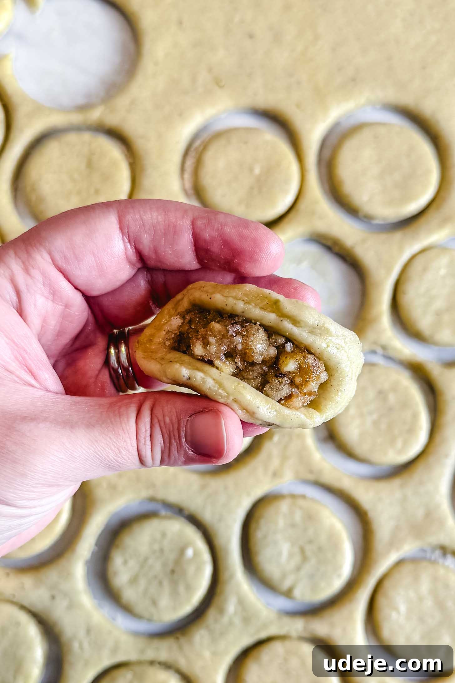 Iraqi Kleicha A Sweet Tradition with Date or Walnut 25 A hand holds a piece of dough filled with a nut mixture, ready to be sealed into kleicha. In the background, dough circles are cut out on a floured surface, preparing for more traditional kleicha treats.