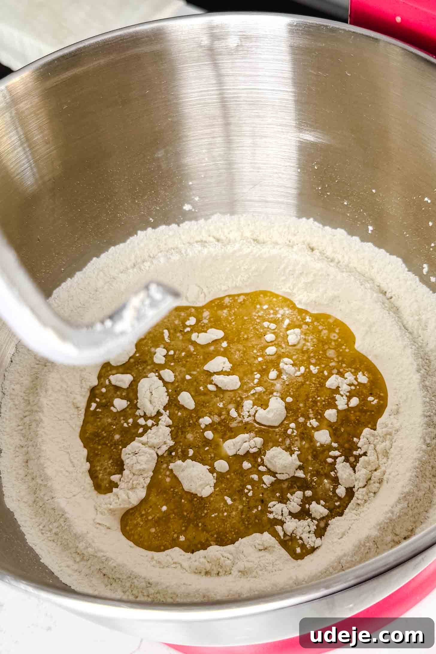 Iraqi Kleicha A Sweet Tradition with Date or Walnut 6 A metal mixing bowl holds ingredients for Kleicha, with a ring of flour and a pool of golden liquid—likely honey or oil—in the center. A dough hook attachment is poised above, ready to start mixing the traditional treat.