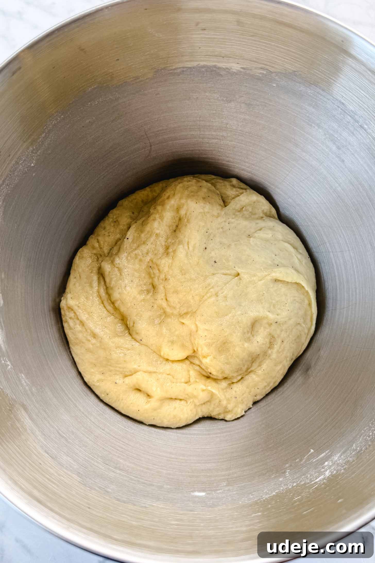 Iraqi Kleicha A Sweet Tradition with Date or Walnut 8 A ball of yellowish Kleicha dough rests at the bottom of a large stainless steel mixing bowl.