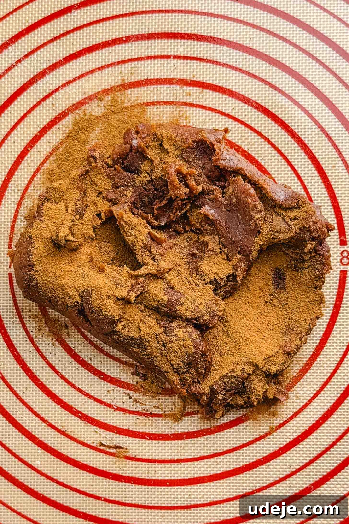 Iraqi Kleicha A Sweet Tradition with Date or Walnut 10 A mound of brown Kleicha dough sprinkled with cinnamon sits on a silicone baking mat with red concentric circles.