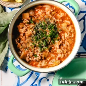 A pot of hearty unstuffed cabbage soup with ground meat, chopped vegetables, and tomato sauce, garnished with fresh herbs.