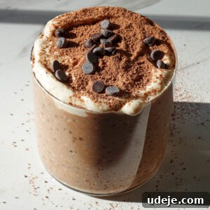 Tiramisu overnight oats in a glass jar topped with yogurt, cocoa powder, and mini chocolate chips