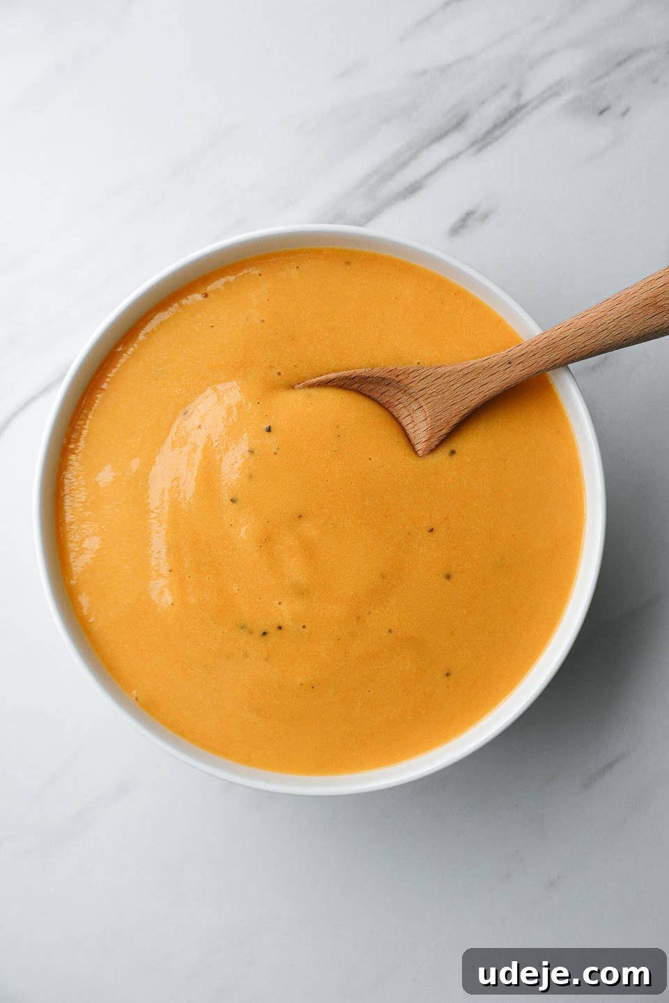 Golden Vegan Cheese Sauce Potato And Carrot Infusion 2 Creamy vegan cheese sauce made with potatoes and carrots in a white bowl, perfect for various dishes.