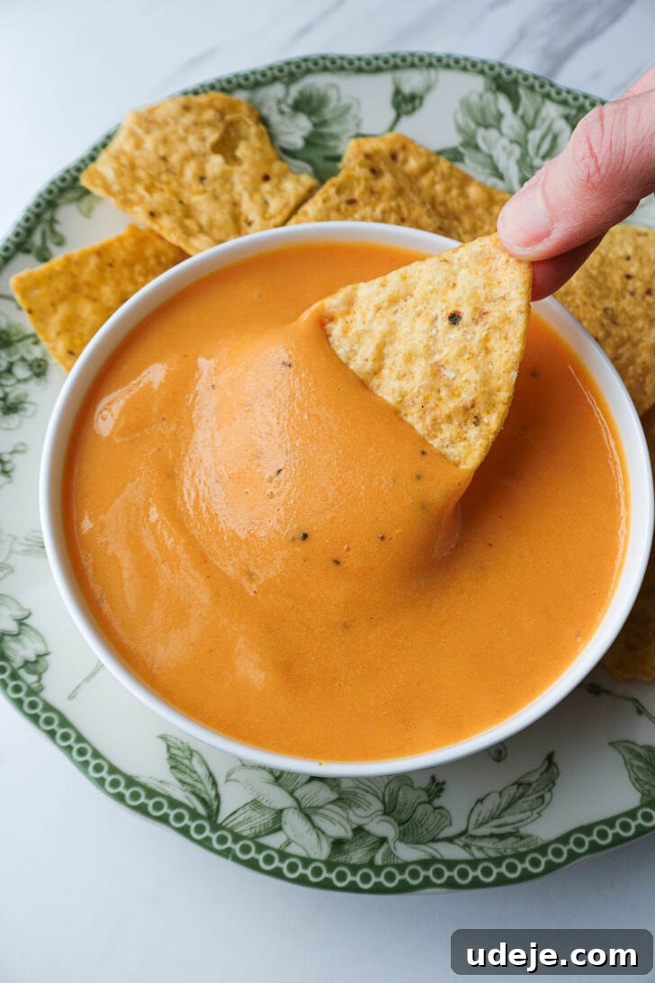 Golden Vegan Cheese Sauce Potato And Carrot Infusion 11 Nut-free vegan cheese sauce served as a queso dip in a white bowl, surrounded by fresh ingredients and tortilla chips