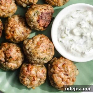 A green plate filled with baked meatballs alongside a small bowl of creamy white dipping sauce, possibly tzatziki.