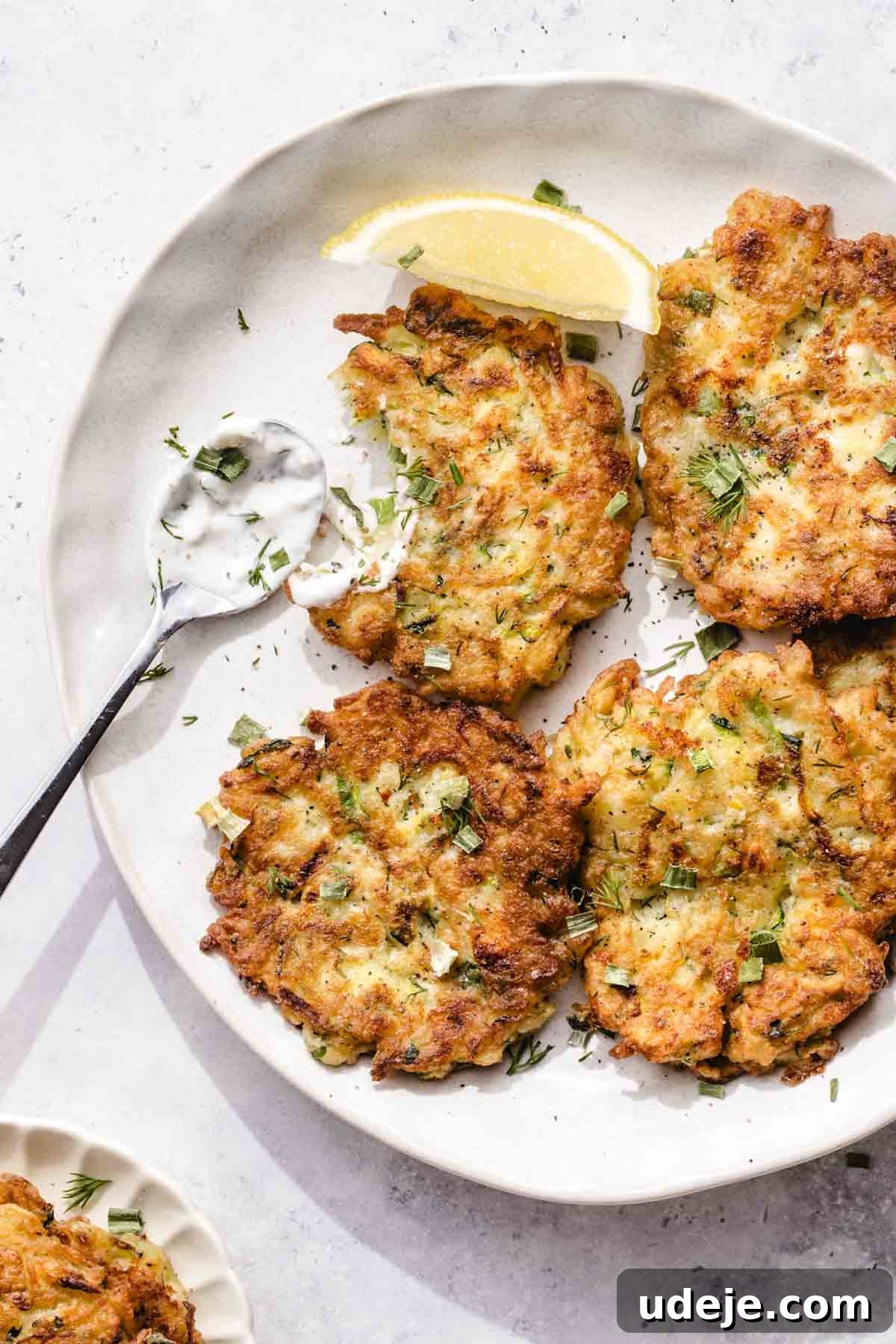 Crispy Turkish Zucchini Feta Fritters 2 A plate with four golden-brown fritters garnished with chopped herbs, a lemon wedge, and a spoonful of creamy dipping sauce on the side. These Turkish Fritters called Mucver, are the perfect appetizer, filled with fresh dill and feta.
