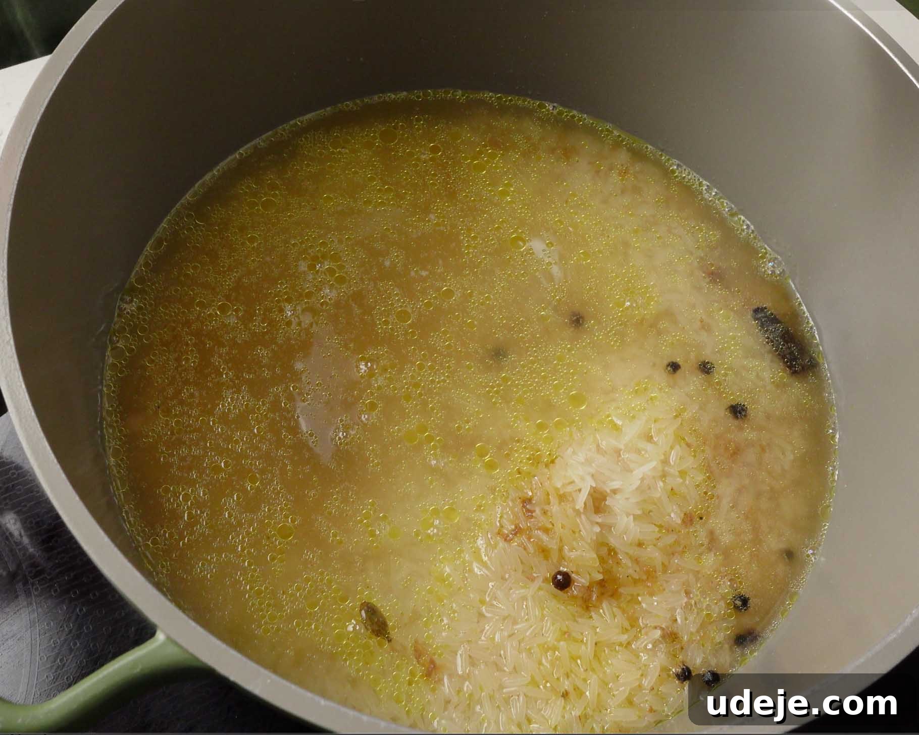Melt-in-Your-Mouth Yemeni Lamb Mandi 16 A pot filled with uncooked rice, whole spices, oil, and water, sitting on a stove and starting to cook. Some rice is clumped together, and oil droplets are visible on the surface.
