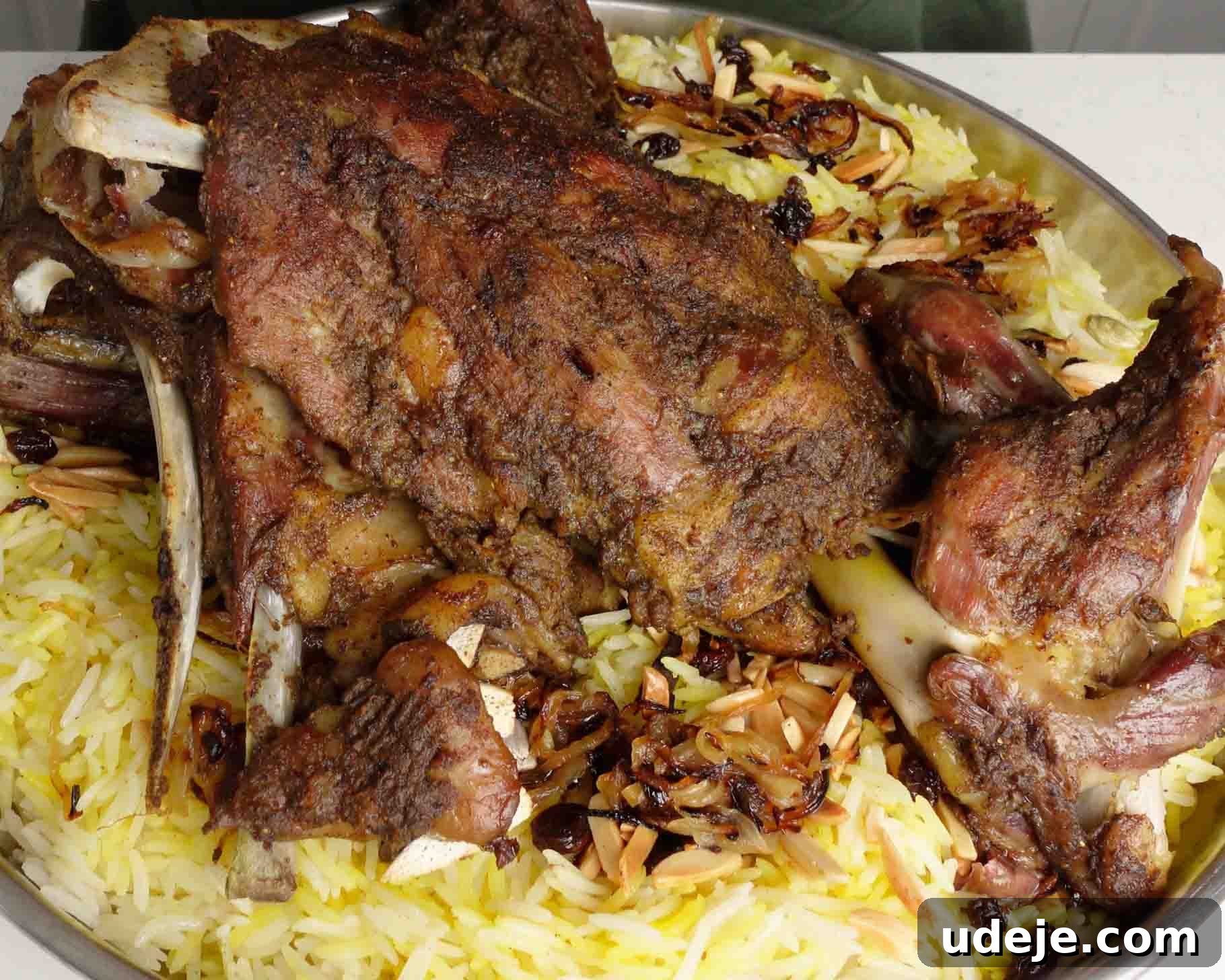 Melt-in-Your-Mouth Yemeni Lamb Mandi 19 A large platter of yellow rice topped with a whole roasted lamb shoulder, garnished with fried slivered almonds and raisins.