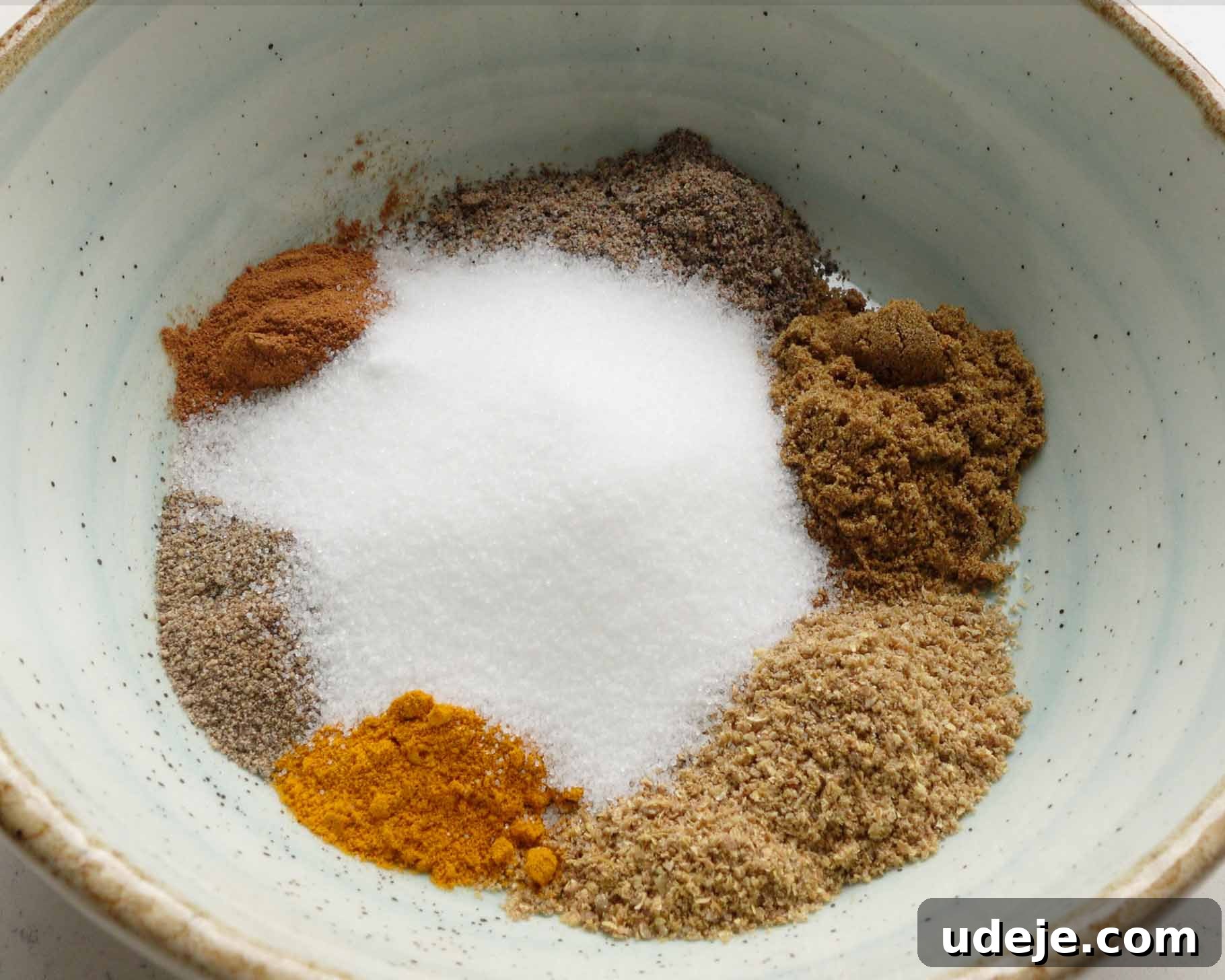 Melt-in-Your-Mouth Yemeni Lamb Mandi 4 A light blue bowl containing separate piles of ground spices, including white granulated sugar, turmeric, black pepper, cinnamon, and other brown and tan spices.