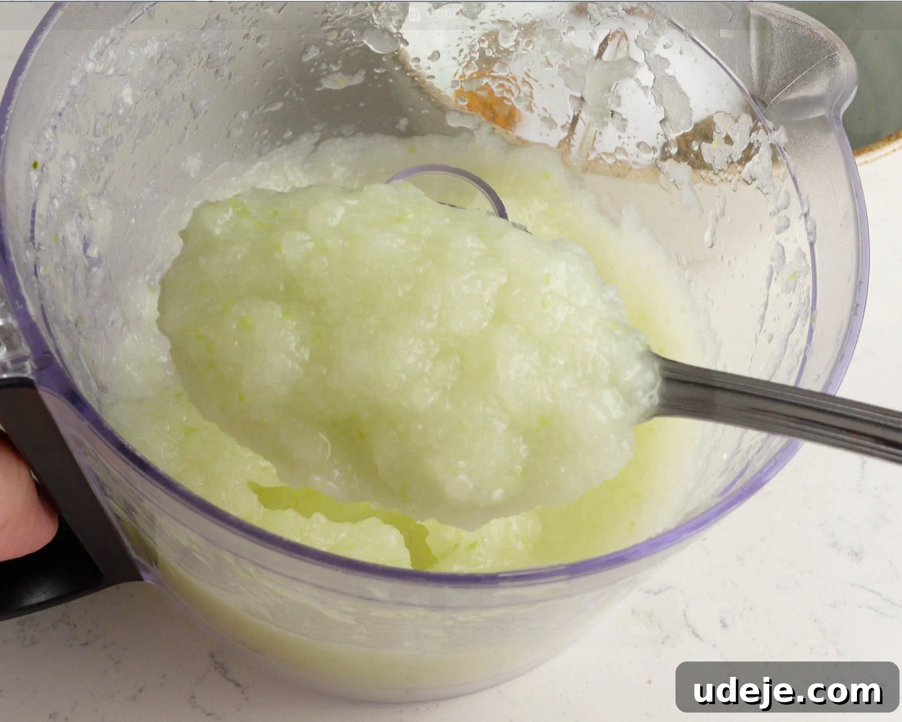 Melt-in-Your-Mouth Yemeni Lamb Mandi 5 A spoon scooping a thick, pale green, slushy mixture from a transparent blender jug on a white countertop.