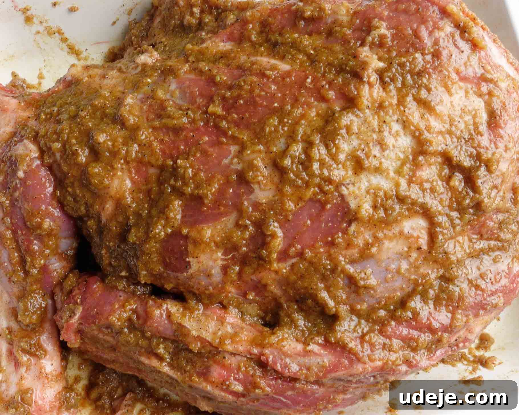 Melt-in-Your-Mouth Yemeni Lamb Mandi 8 Close-up of a large piece of raw lamb coated with a thick, brownish marinade or spice rub, resting in a white dish.