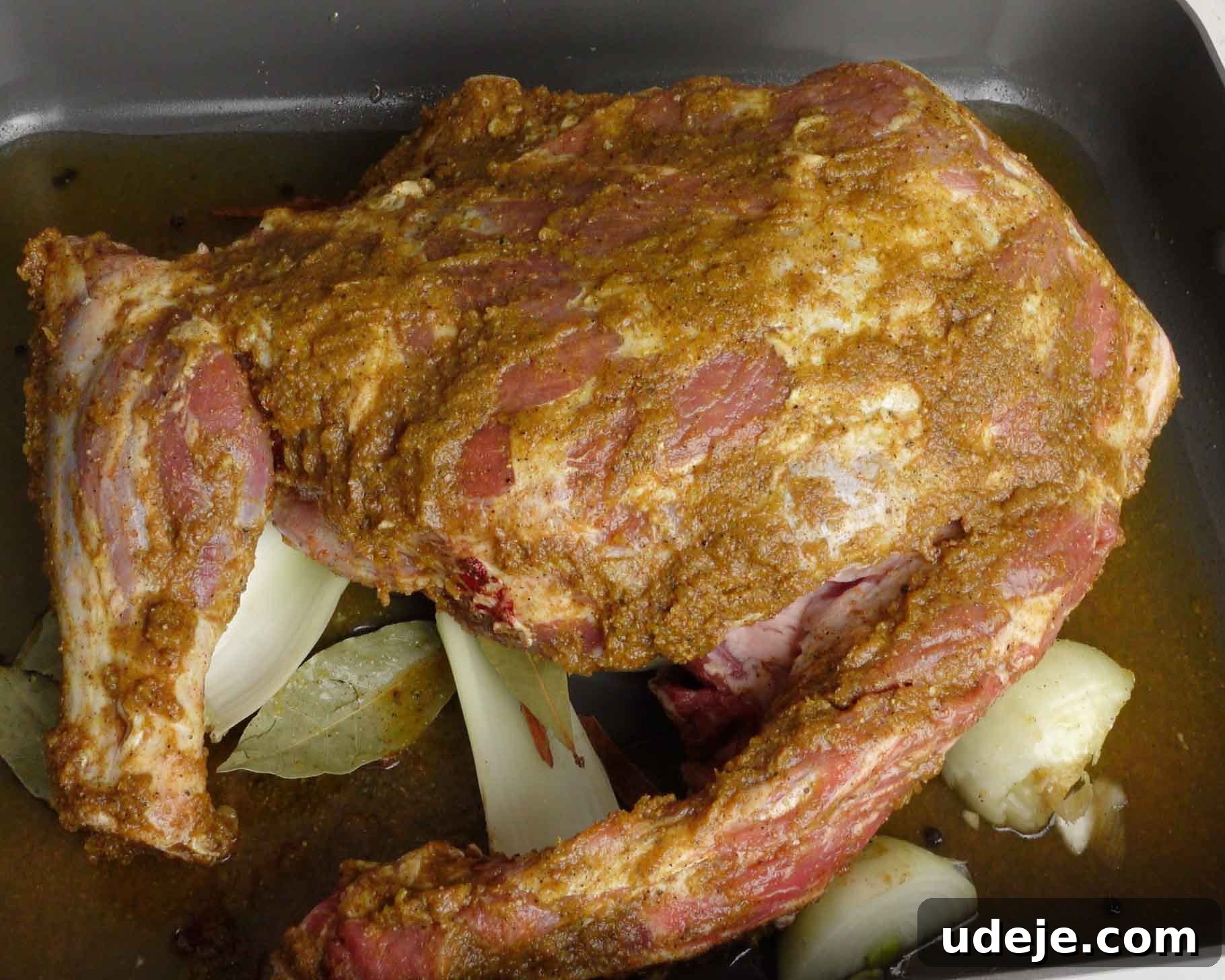 Melt-in-Your-Mouth Yemeni Lamb Mandi 9 A marinated piece of lamb, rests on chopped onions and bay leaves in a roasting pan, ready to be cooked.