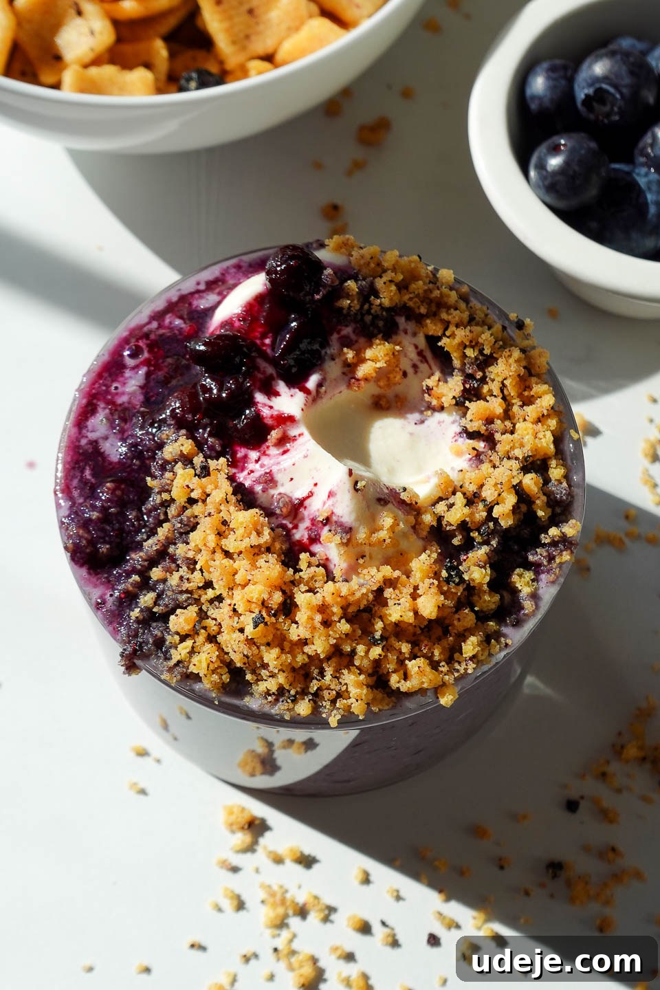 Blueberry Muffin Bliss Overnight Oats 2 Blueberry muffin overnight oats in a glass jar topped with vegan yogurt, blueberry compote, and crushed protein cereal