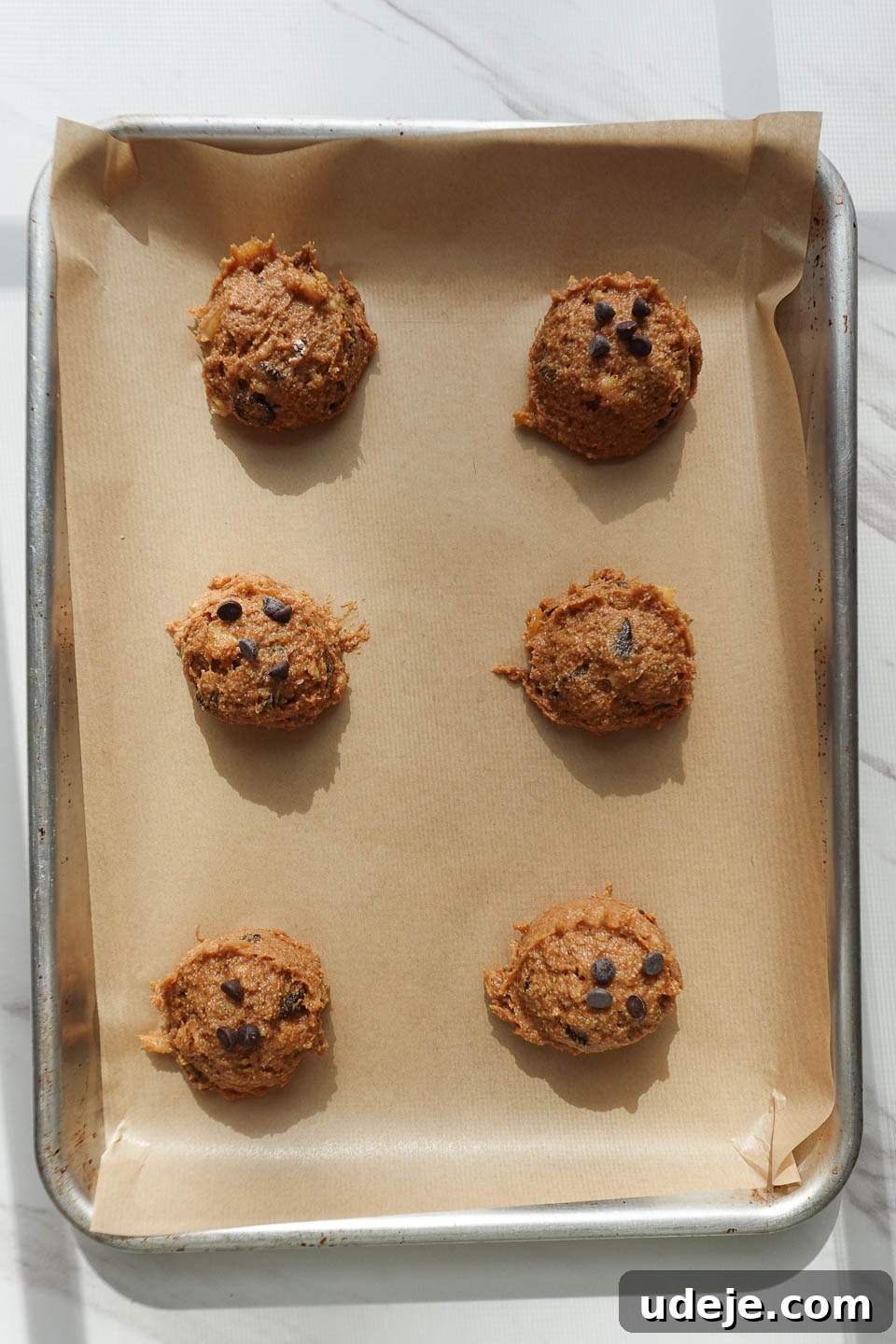 Soft-Baked Vegan Banana Bread Cookies 9 Uniformly scooped balls of vegan banana bread cookie dough neatly arranged on a parchment-lined baking sheet, spaced out and ready for the oven.