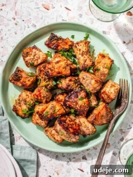 Air Fryer Salmon bites on a light green plate garnished with chopped parsley on a green tea towel, a light green glass with water, a metal fork in the plate on a pink terrazzo background