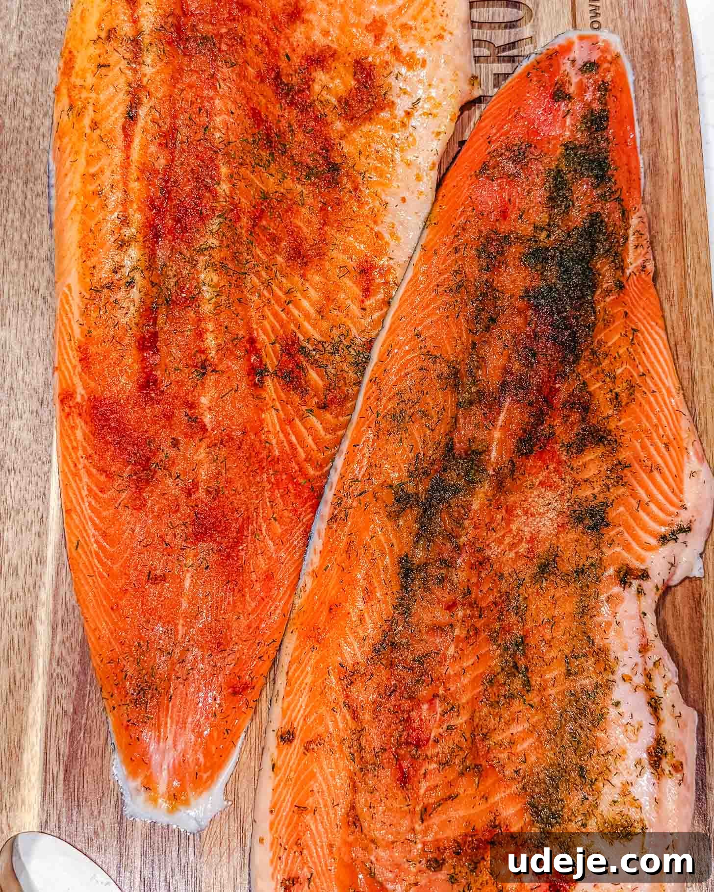 Sheet Pan Rainbow Trout with Crispy Potatoes and Lemon 3 Two raw salmon fillets on a wooden cutting board, seasoned with various spices and herbs, showing bright orange flesh and visible seasoning.