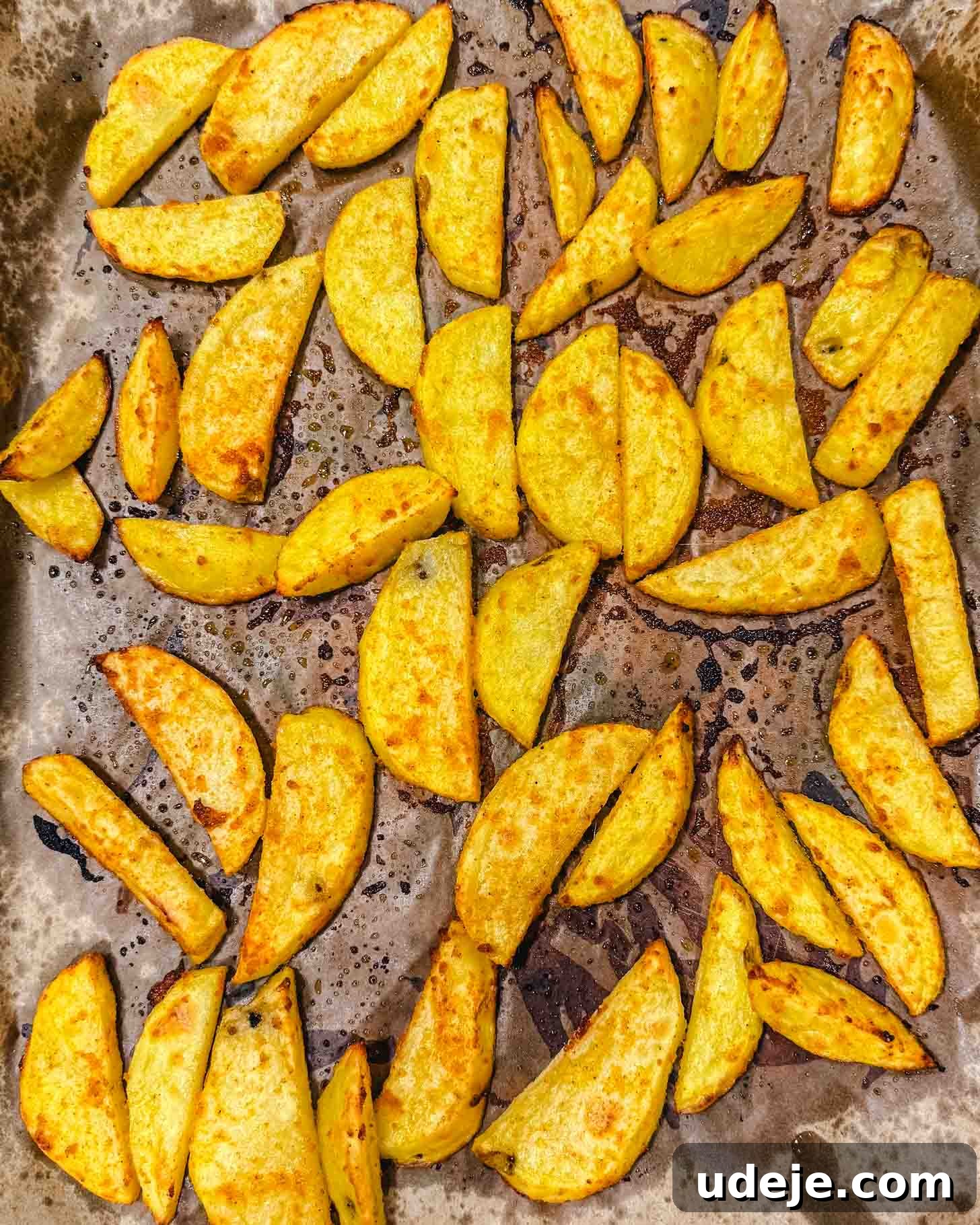 Sheet Pan Rainbow Trout with Crispy Potatoes and Lemon 4 Golden, crispy potato wedges are spread out on a baking sheet lined with parchment paper, showing some browning and oily spots from roasting.