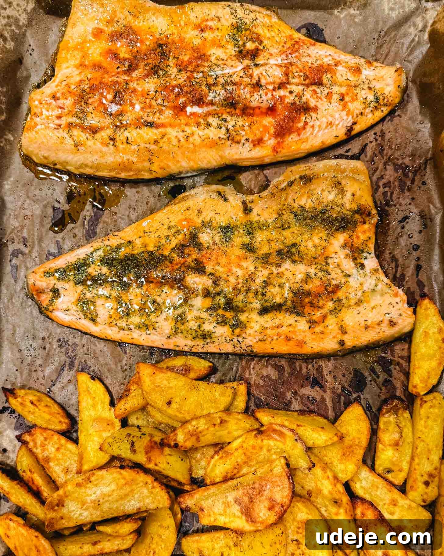 Sheet Pan Rainbow Trout with Crispy Potatoes and Lemon 6 Two seasoned salmon fillets and a pile of golden roasted potato wedges on a parchment-lined baking tray, fresh from the oven.
