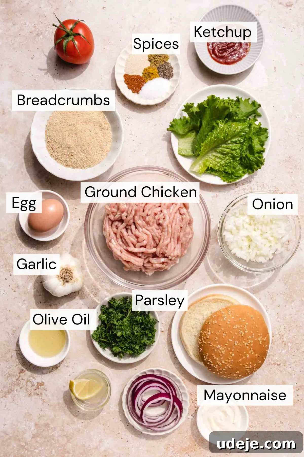 Middle Eastern Juicy Ground Chicken Burger Recipe 3 Labeled ingredients for chicken burgers are arranged on a countertop, including ground chicken, lettuce, onion, breadcrumbs, parsley, egg, garlic, olive oil, spices, ketchup, mayonnaise, and a burger bun.