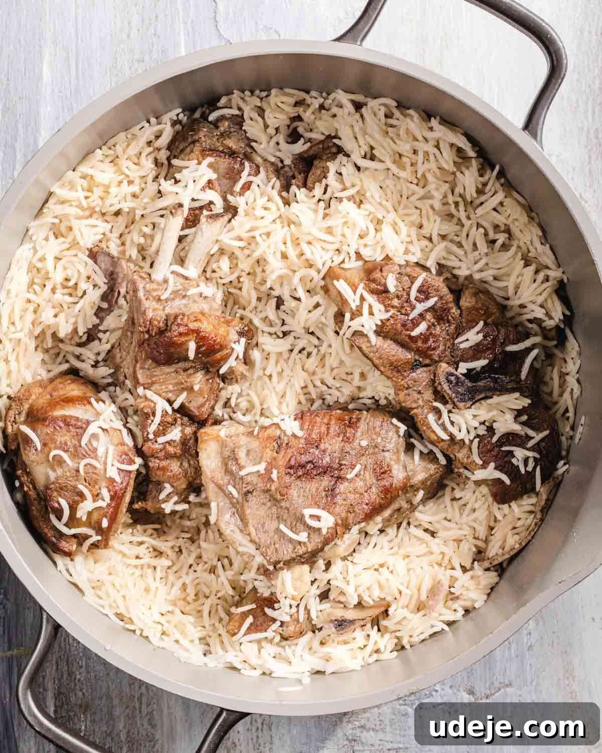 Kabuli Pulao: Slow-Cooked Afghan Lamb and Spiced Rice Recipe 12 A large metal pot filled with cooked basmati rice and several browned pieces of meat, likely lamb or beef, on a light-colored surface.
