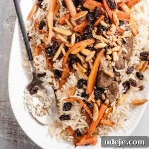 Kabuli Pulao: Slow-Cooked Afghan Lamb and Spiced Rice Recipe 14 A white oval plate of rice topped with sautéed carrots, slivered almonds, raisins, and pieces of meat. A serving spoon rests on the side of the plate.