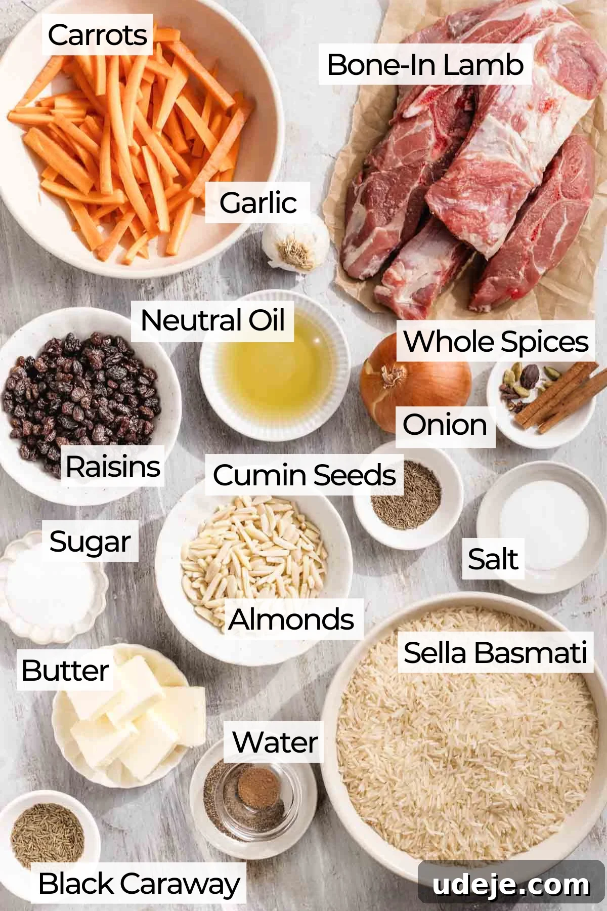 Kabuli Pulao: Slow-Cooked Afghan Lamb and Spiced Rice Recipe 3 Various labeled ingredients for a recipe are arranged on a light surface, including bone-in lamb, carrots, garlic, basmati rice, whole spices, onion, oil, raisins, cumin seeds, almonds, salt, sugar, butter, water, and black caraway.