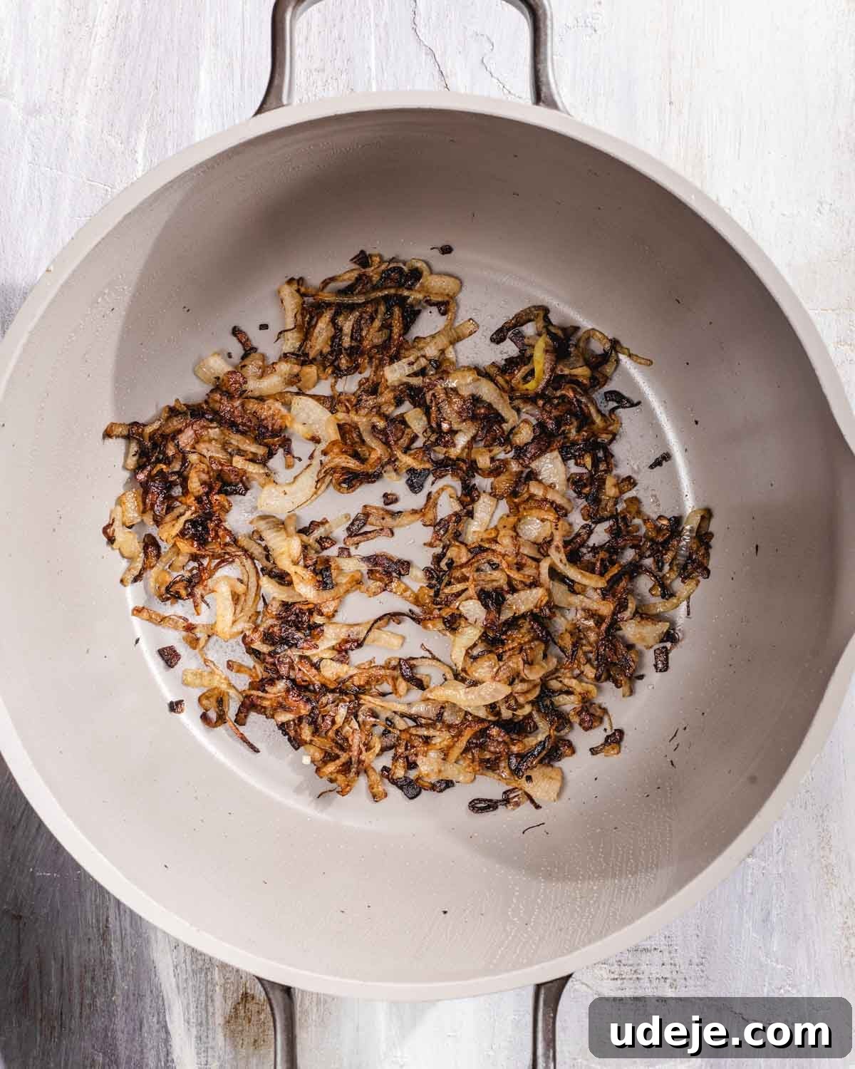 Kabuli Pulao: Slow-Cooked Afghan Lamb and Spiced Rice Recipe 7 Sliced onions being caramelized in a light-colored, round pot on a white surface, with some pieces browned and others golden.