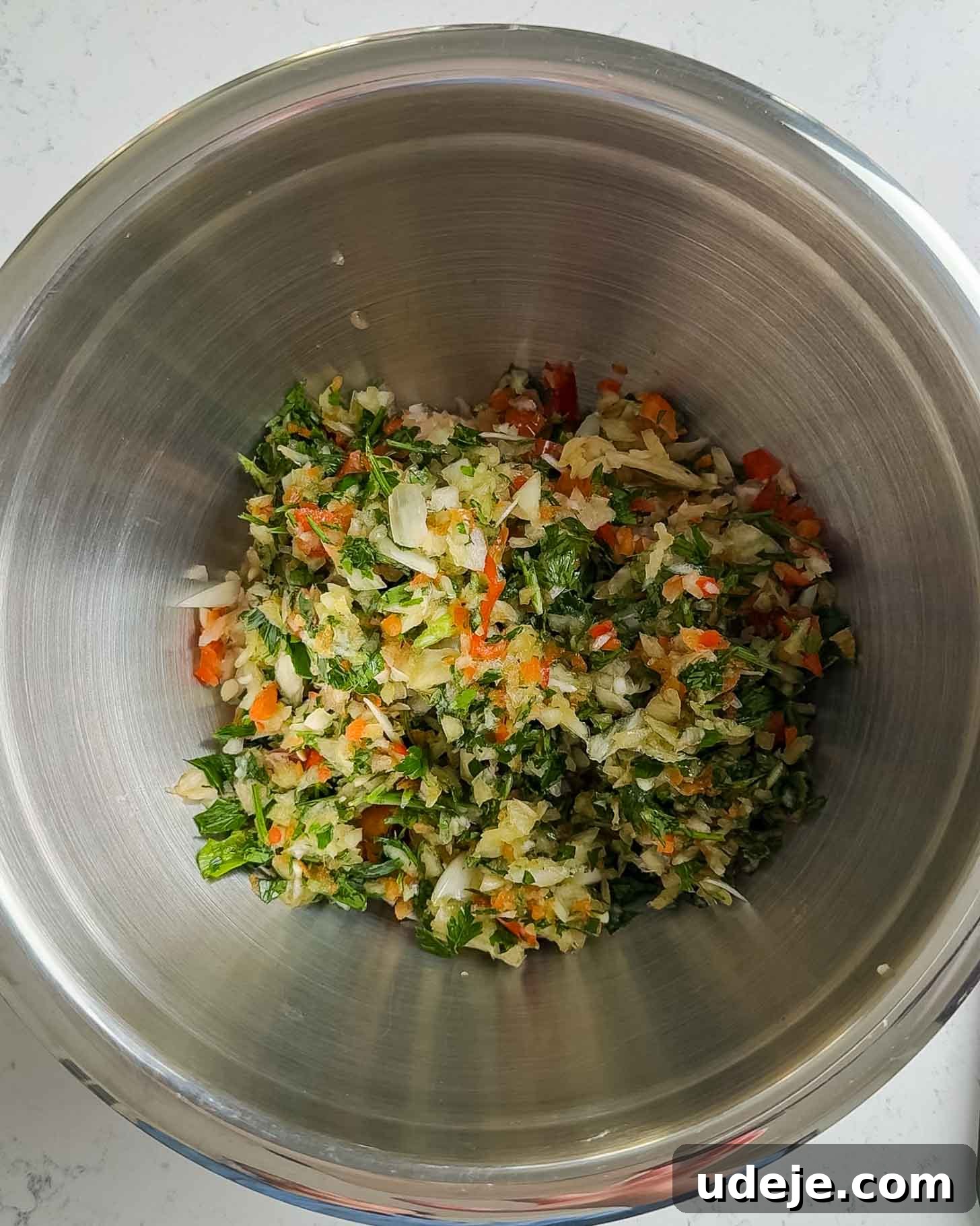 Juicy Ground Beef Sheet Pan Kebabs: Quick Oven Dinner 4 A metal mixing bowl containing a colorful chopped vegetable mixture, including green leafy herbs, orange carrots, red bell peppers, and white cabbage, set on a light-colored countertop.