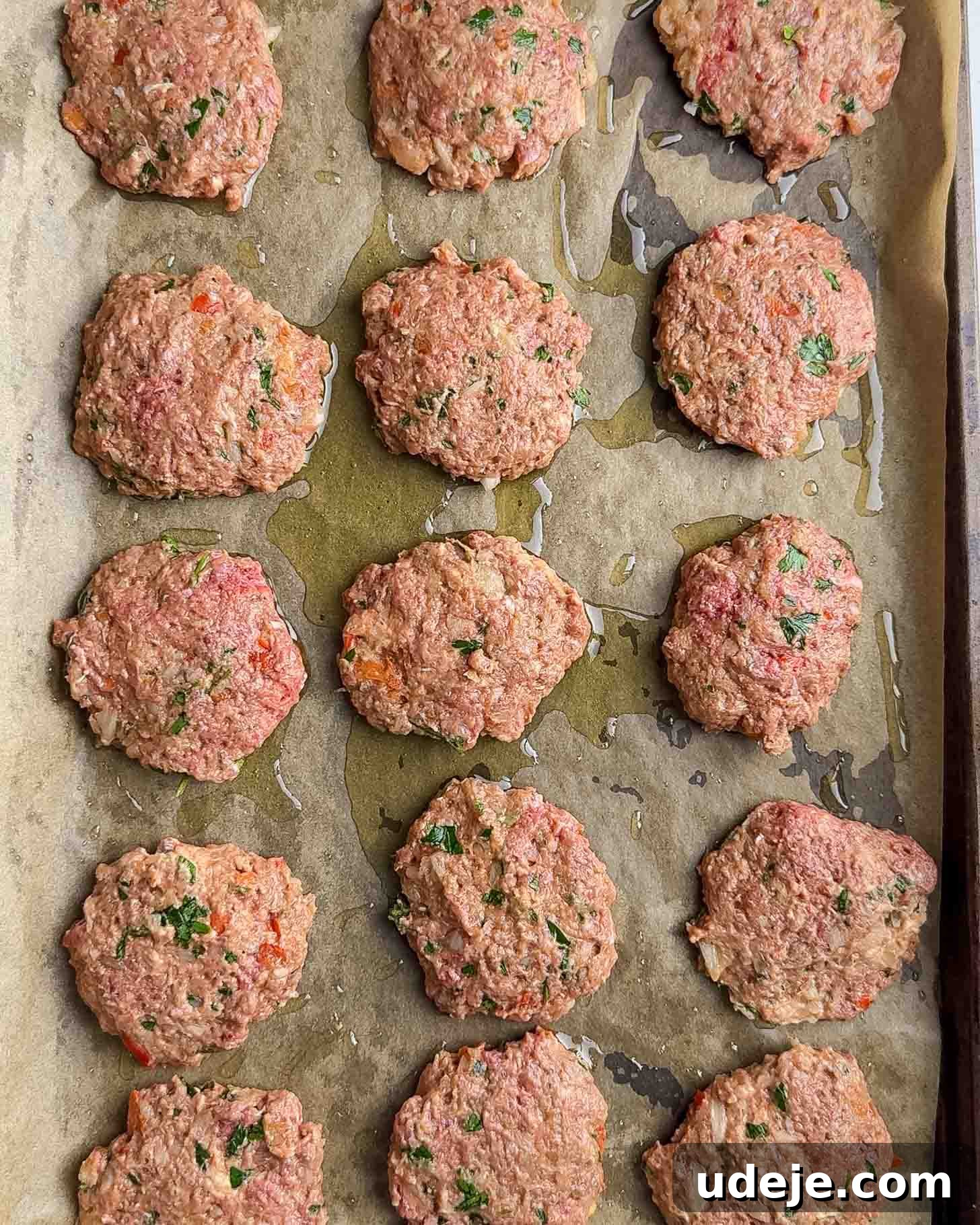 Juicy Ground Beef Sheet Pan Kebabs: Quick Oven Dinner 7 Raw, seasoned meat patties arranged in rows on a baking sheet lined with parchment paper and drizzled with oil, ready to be cooked.
