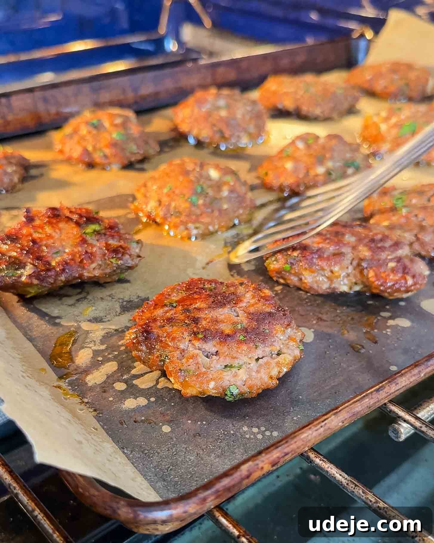 Juicy Ground Beef Sheet Pan Kebabs: Quick Oven Dinner 8 Several browned sausage patties are baking on a parchment-lined baking sheet in an oven. A fork is lifting one of the patties, showing their crispy, cooked texture with some oil around them.