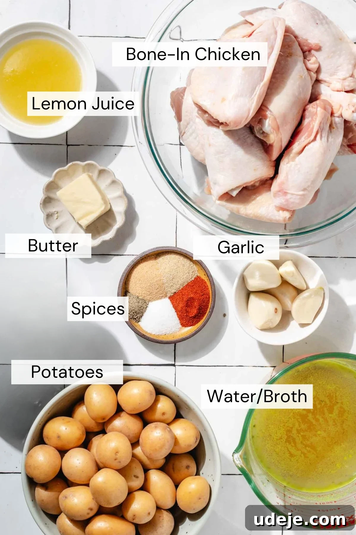 Roasted Lemon Garlic Chicken with Irresistible Pan Juices 4 A flat lay of labeled ingredients including bone-in chicken, lemon juice, butter, spices, garlic, potatoes, and a measuring cup of water or broth on a white surface.