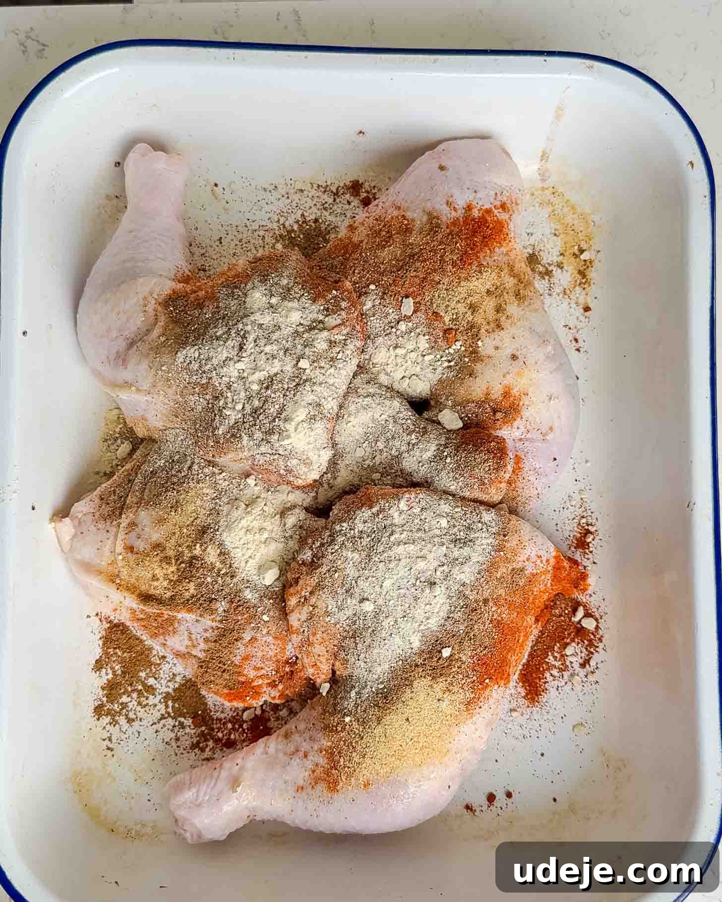 Roasted Lemon Garlic Chicken with Irresistible Pan Juices 5 Raw chicken legs in a white tray, sprinkled with various spices and flour, ready for seasoning or marinating.