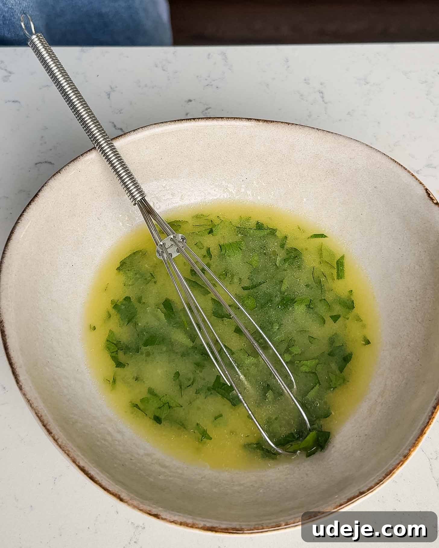 Roasted Lemon Garlic Chicken with Irresistible Pan Juices 7 A white bowl with a metal whisk resting inside, containing a green herb vinaigrette or salad dressing on a white countertop.