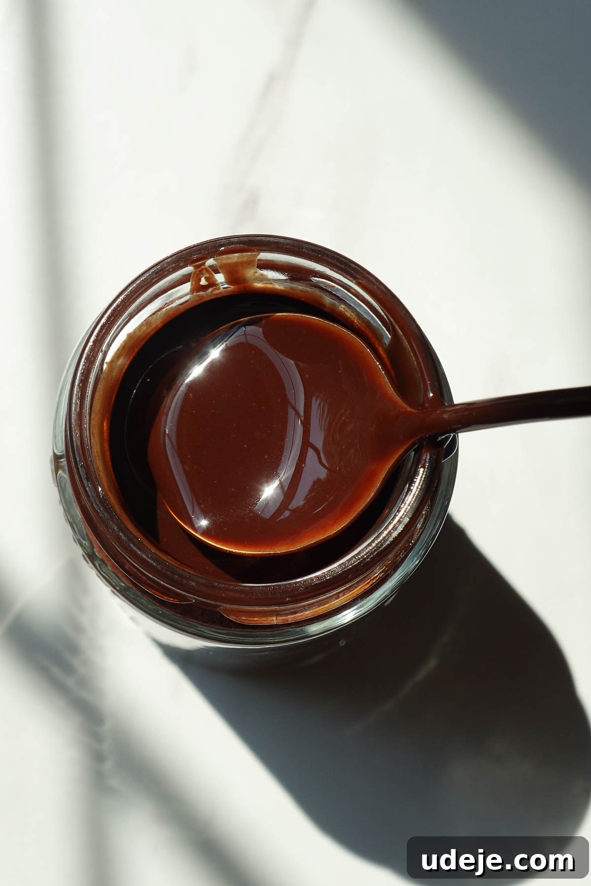 Healthy homemade chocolate syrup in a glass jar with a spoon.