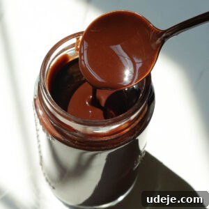 Homemade chocolate syrup drizzled from a spoon, showing its thick and smooth chocolate texture.