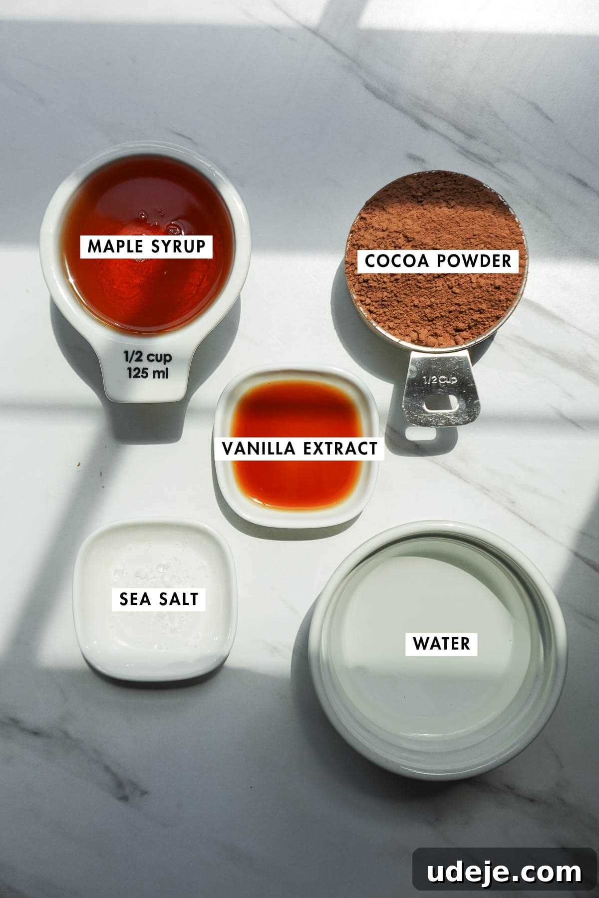 Ingredients for homemade chocolate syrup including cocoa powder, maple syrup, vanilla extract, and sea salt.