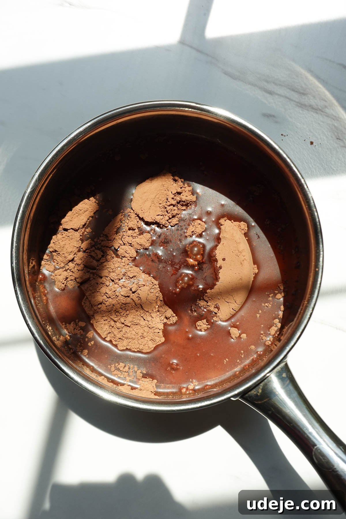 Cocoa powder, maple syrup, water, vanilla extract, and sea salt added to a saucepan to make homemade chocolate syrup.