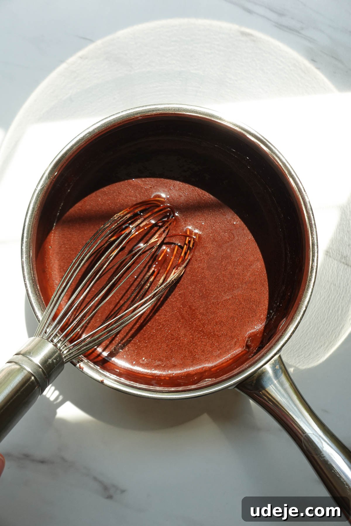 Whisking cocoa powder and other ingredients together in a saucepan to make chocolate syrup.