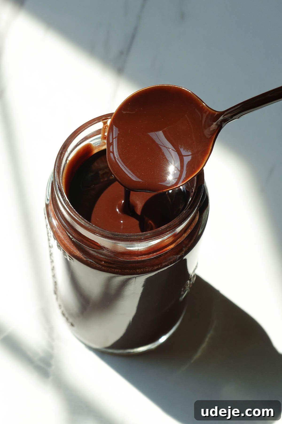 Homemade chocolate syrup drizzled from a spoon, showing its thick and smooth chocolate texture.