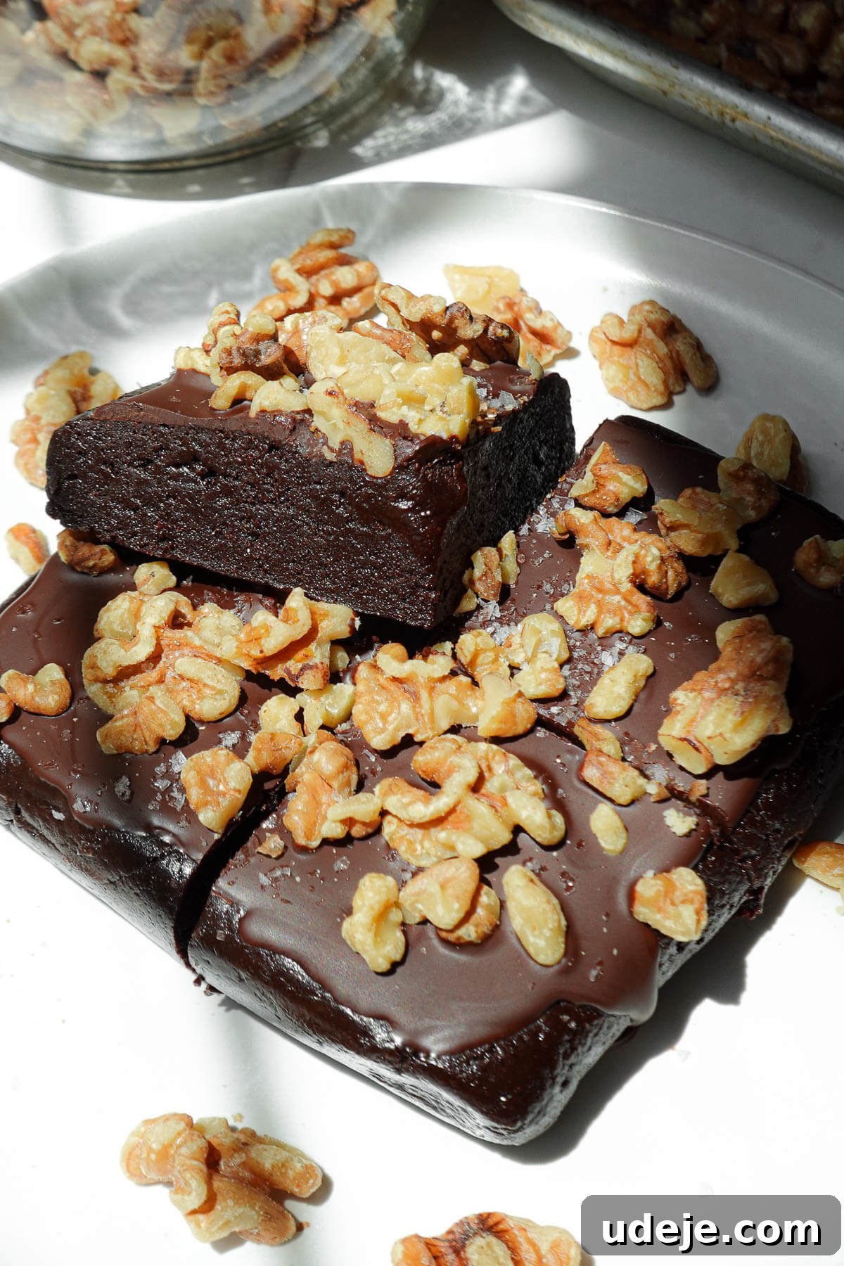 Fudgy Walnut Date Brownies Recipe 2 Sliced walnut date brownies on a plate, topped with vegan chocolate and walnuts.
