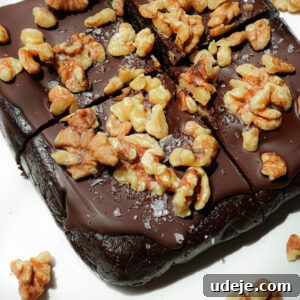 Sliced walnut date brownies on a plate, topped with vegan chocolate and walnuts.