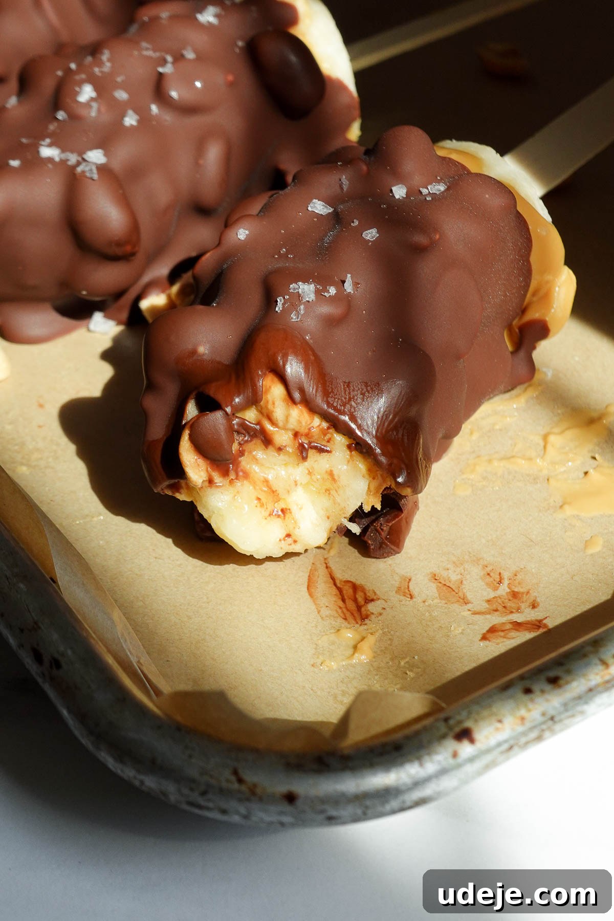 Snickers-Stuffed Frozen Banana Pops 11 Banana pops with a bite taken showing layers