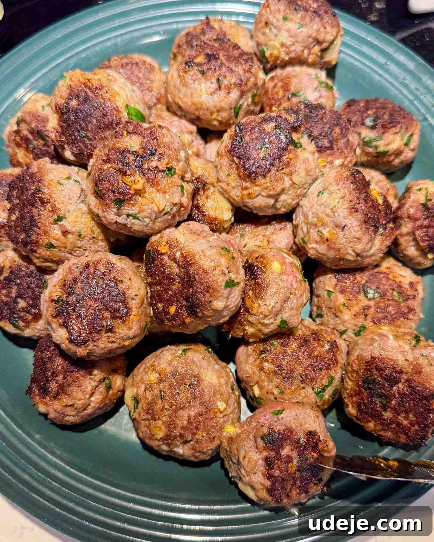One-Pot Lemony Greek Meatballs and Potatoes (Stovetop) 5 A teal plate piled with browned homemade meatballs, garnished with bits of herbs and possibly cheese, showing a crispy, seared exterior.