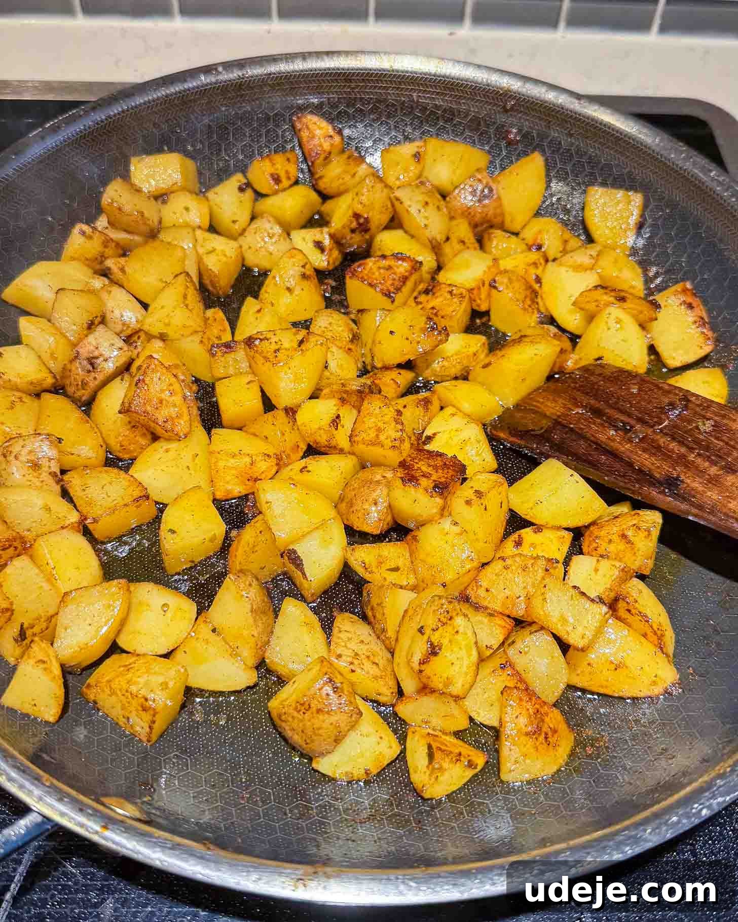 One-Pot Lemony Greek Meatballs and Potatoes (Stovetop) 6 Diced potatoes being sautéed in a frying pan with seasoning; a wooden spatula rests on the side of the pan.