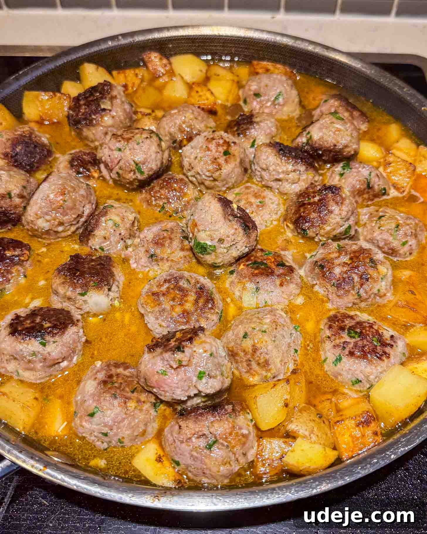 One-Pot Lemony Greek Meatballs and Potatoes (Stovetop) 7 A pan filled with browned meatballs and cubed potatoes simmering in a golden, seasoned sauce on a stovetop.