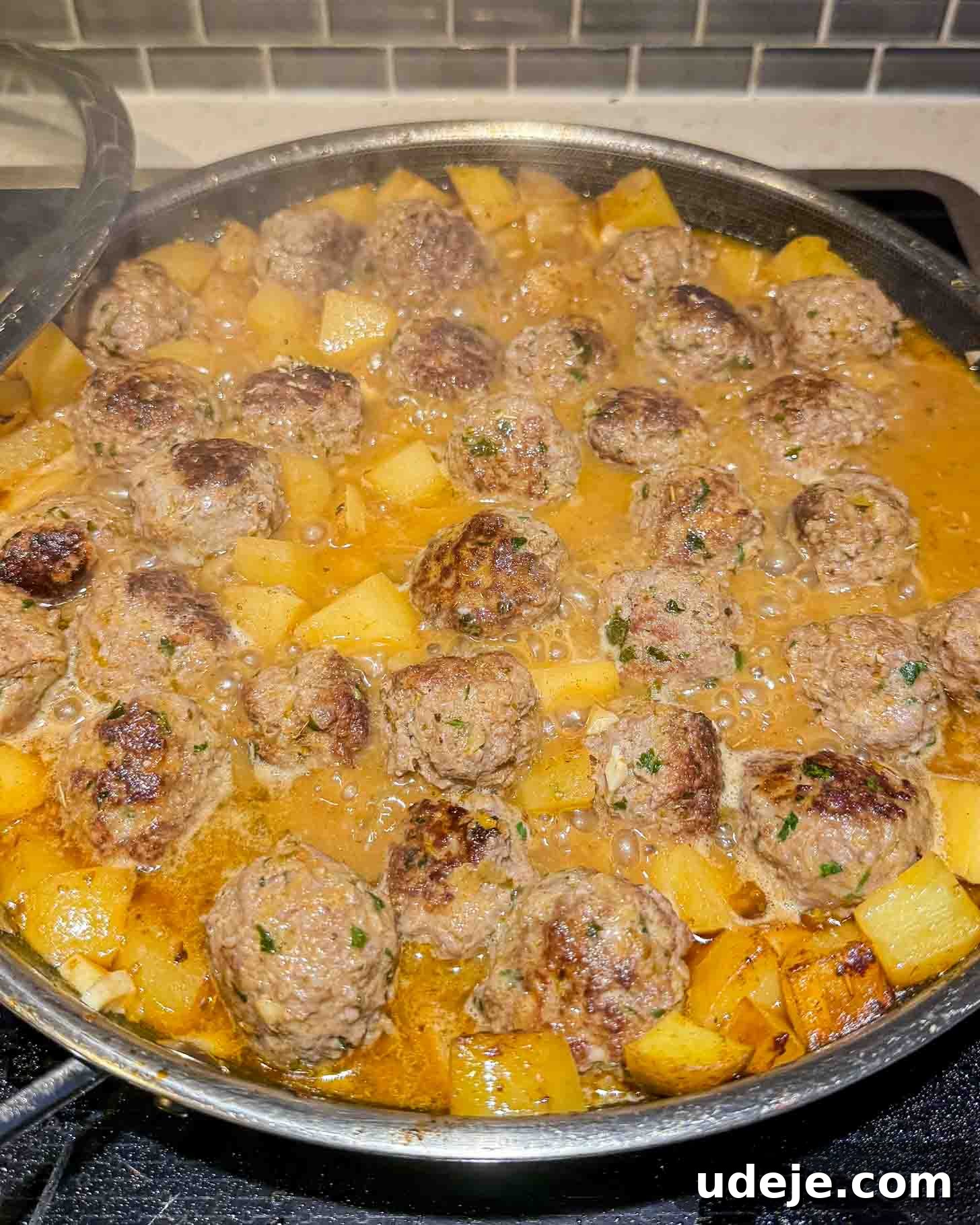 One-Pot Lemony Greek Meatballs and Potatoes (Stovetop) 8 Meatballs and cubed potatoes simmer in a rich brown sauce in a large skillet on a stovetop, with chopped herbs sprinkled on top.