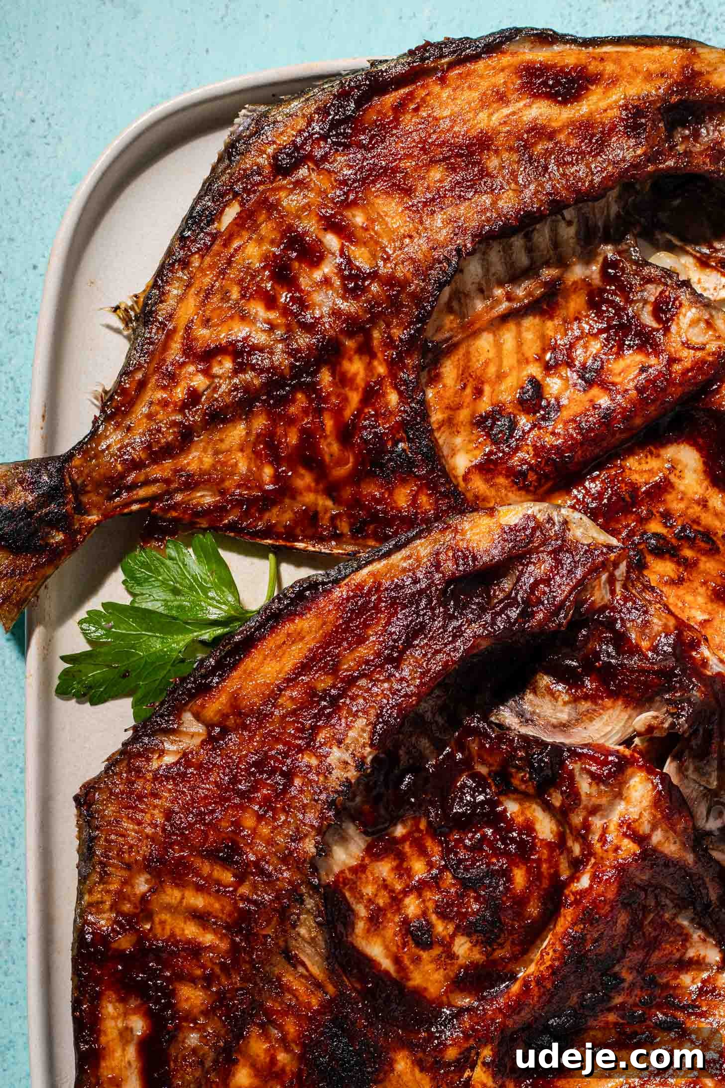 Grilled fish with crispy, golden-brown skin on a white plate, garnished with fresh parsley.