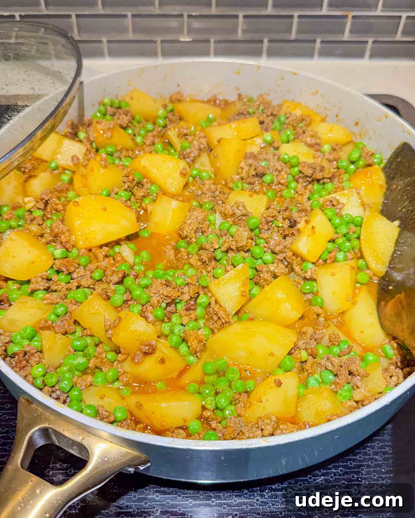 Iraqi-Style Ground Beef and Potato Curry 10 A skillet filled with cooked ground meat, diced potatoes, and green peas in a savory sauce sits on a stovetop, ready to serve.