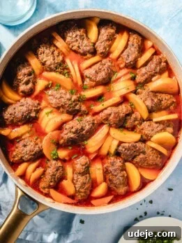 A skillet filled with oval-shaped meat patties and sliced potatoes cooked in a red tomato sauce, garnished with chopped herbs.